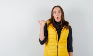 La doudoune sans manche : La nouvelle veste incontournable du dressing des femmes Femme surprise en gilet jaune pointant derrière elle