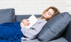Faites le choix d’un plaid chauffant pour vos soirées d’hiver Femme endormie sur canapé avec livre