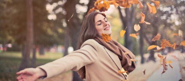 Femme souriante parmi feuilles d’automne au parc