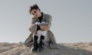 Parkas pour femmes : Comment trouver le modèle parfait pour votre silhouette ? Femme assise sur dune, paysage désertique