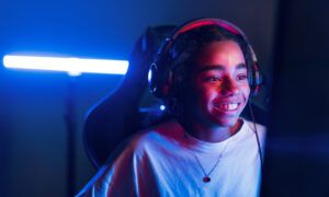 Cloud II vs Cloud Stinger : Quel casque HyperX s'intègre le mieux dans un setup gaming ? Jeune femme souriante avec casque devant écran lumineux