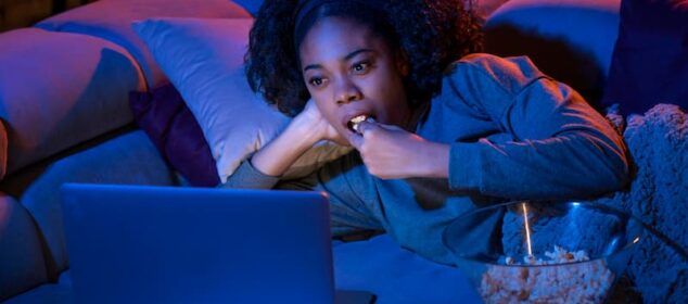 Femme regardant un ordinateur portable en mangeant du popcorn